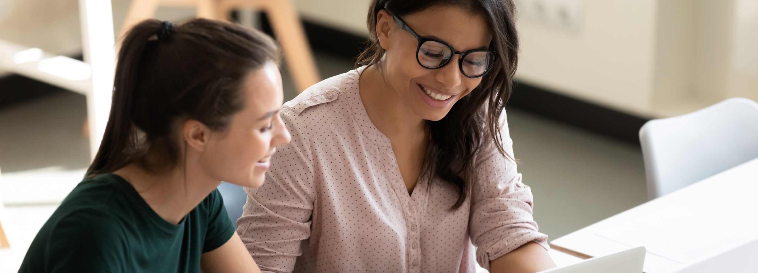 Das Bild zeigt zwei lächelnde Frauen, die gemeinsam an einem Laptop arbeiten und eine positive und kollaborative Arbeitsatmosphäre ausstrahlen.